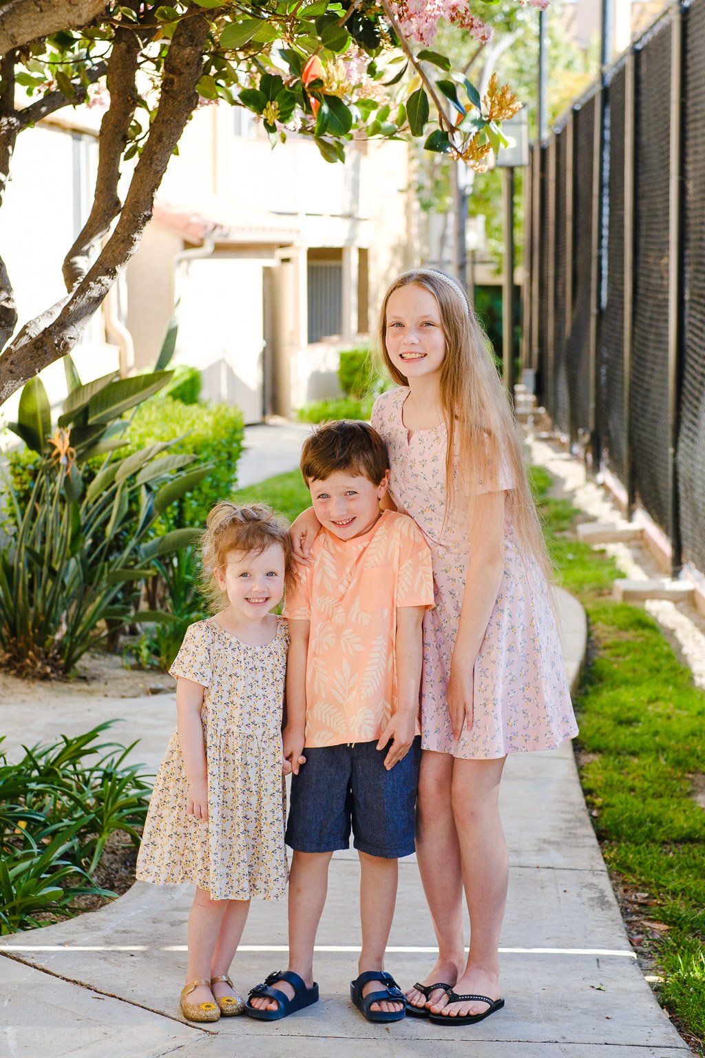 A photo of my three kids on a sunny day under a blossoming tree.