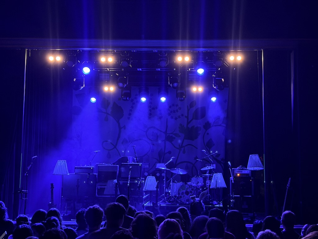 The Beths stage set up with a bunch of floor and table lamps everywhere, and their vines and floral backdrop